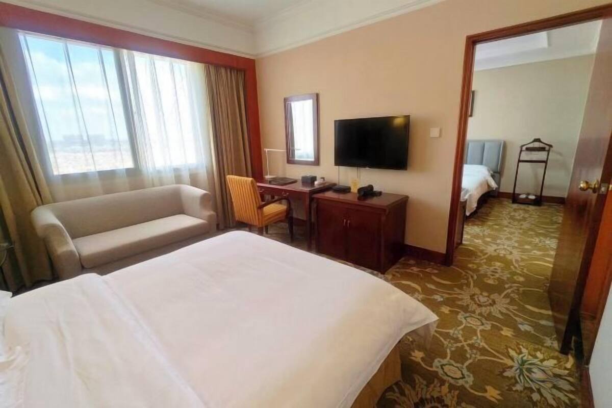 Ein Hotelzimmer mit einem großen Bett, einem Schreibtisch mit Stuhl, einem Fernseher und Blick auf die Stadt durch das Fenster.