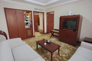 Una habitación de hotel con sofá, televisión, armario y alfombra estampada.