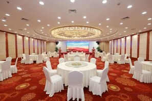Een feestzaal met ronde tafels en stoelen, een groot scherm en een vloer belegd met rood tapijt.