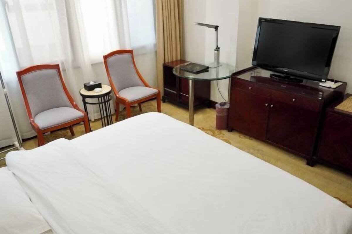 Ein Hotelzimmer mit einem Bett, zwei Sesseln, einem kleinen Tisch mit einer Lampe, einem Fernseher und einem Schrank.