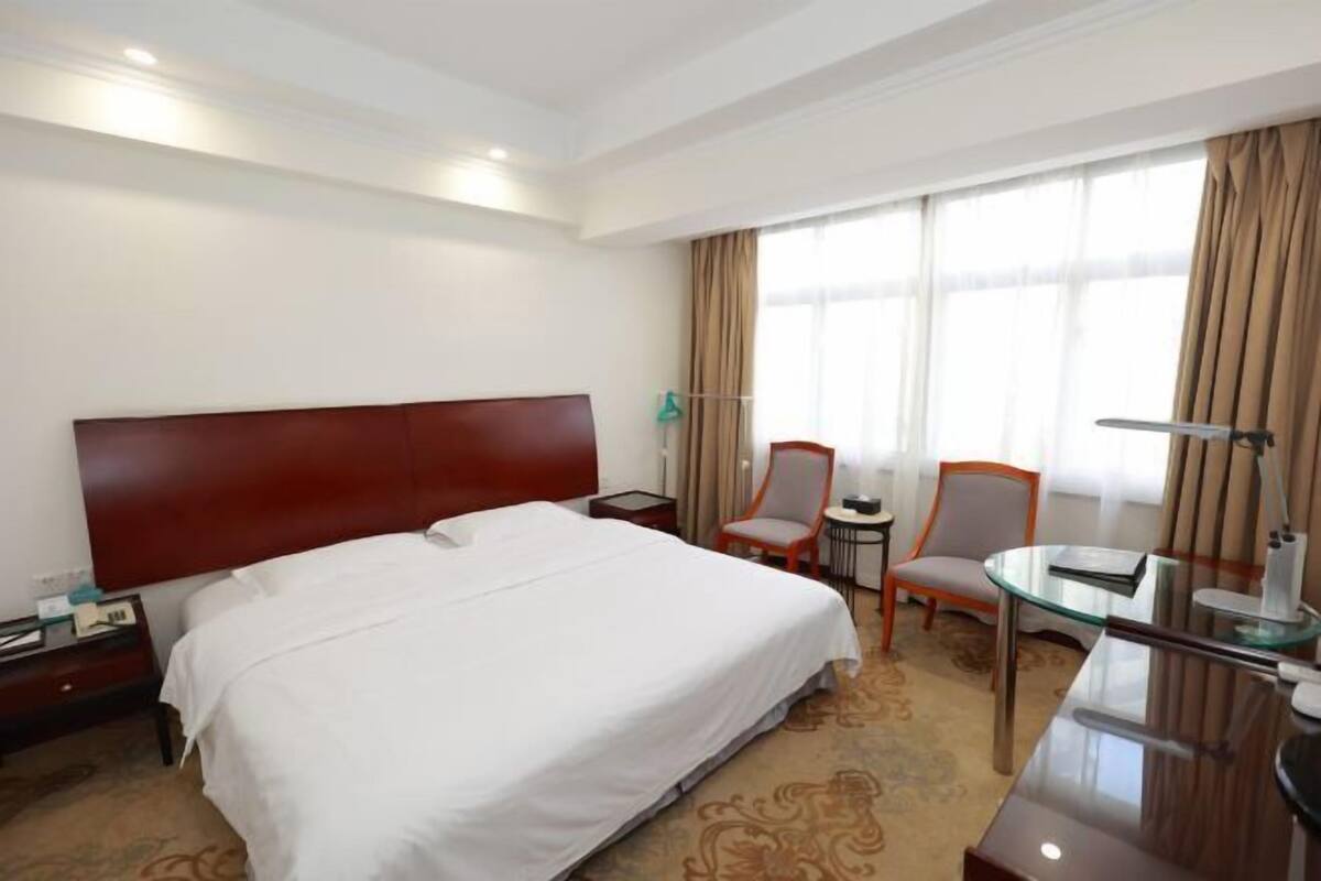 Ein Hotelzimmer mit einem großen Bett, zwei Stühlen, einem kleinen Tisch und einem Schreibtisch mit einer Lampe.