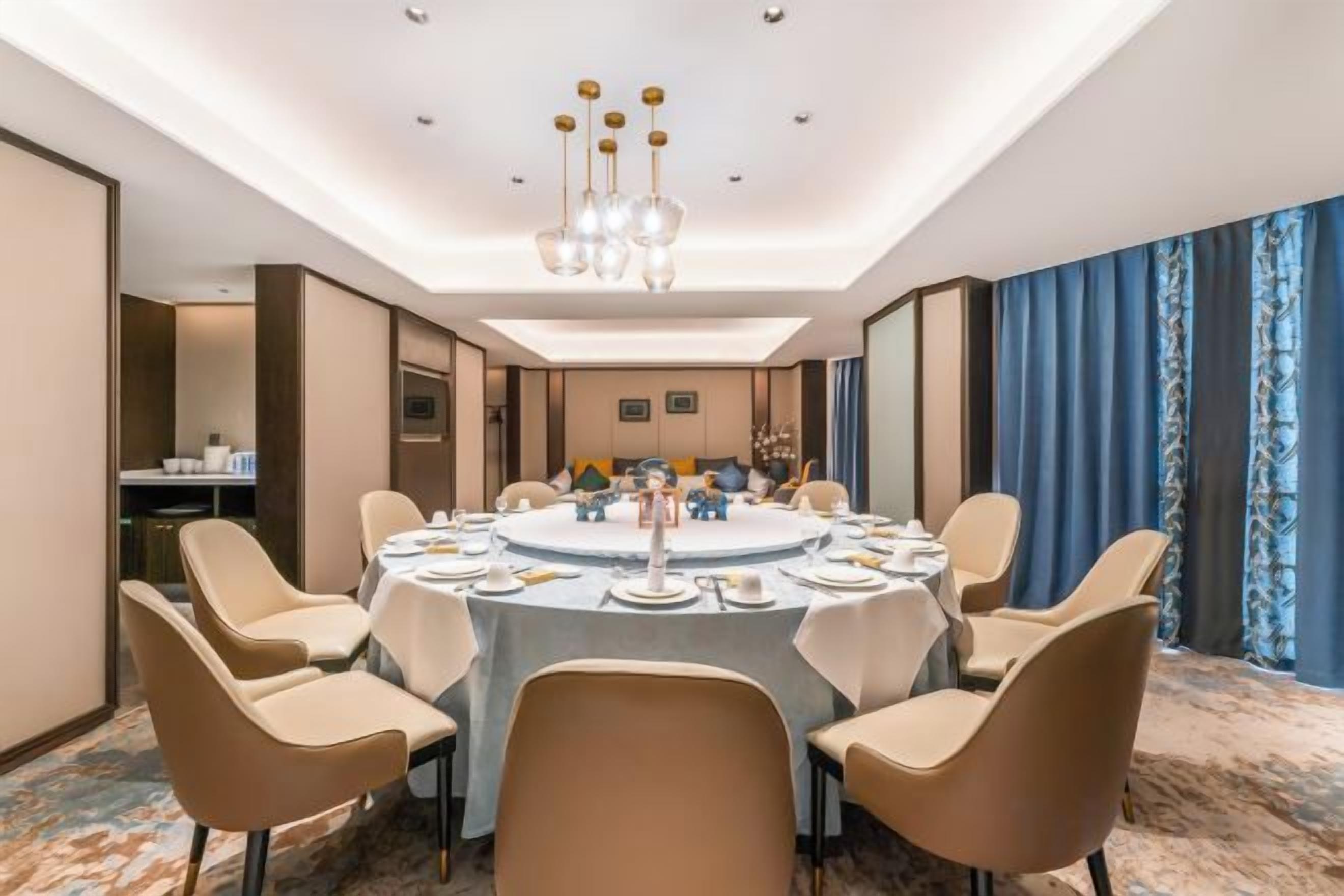 Une salle de conférence avec une table ronde, des chaises de couleur beige et un lustre.