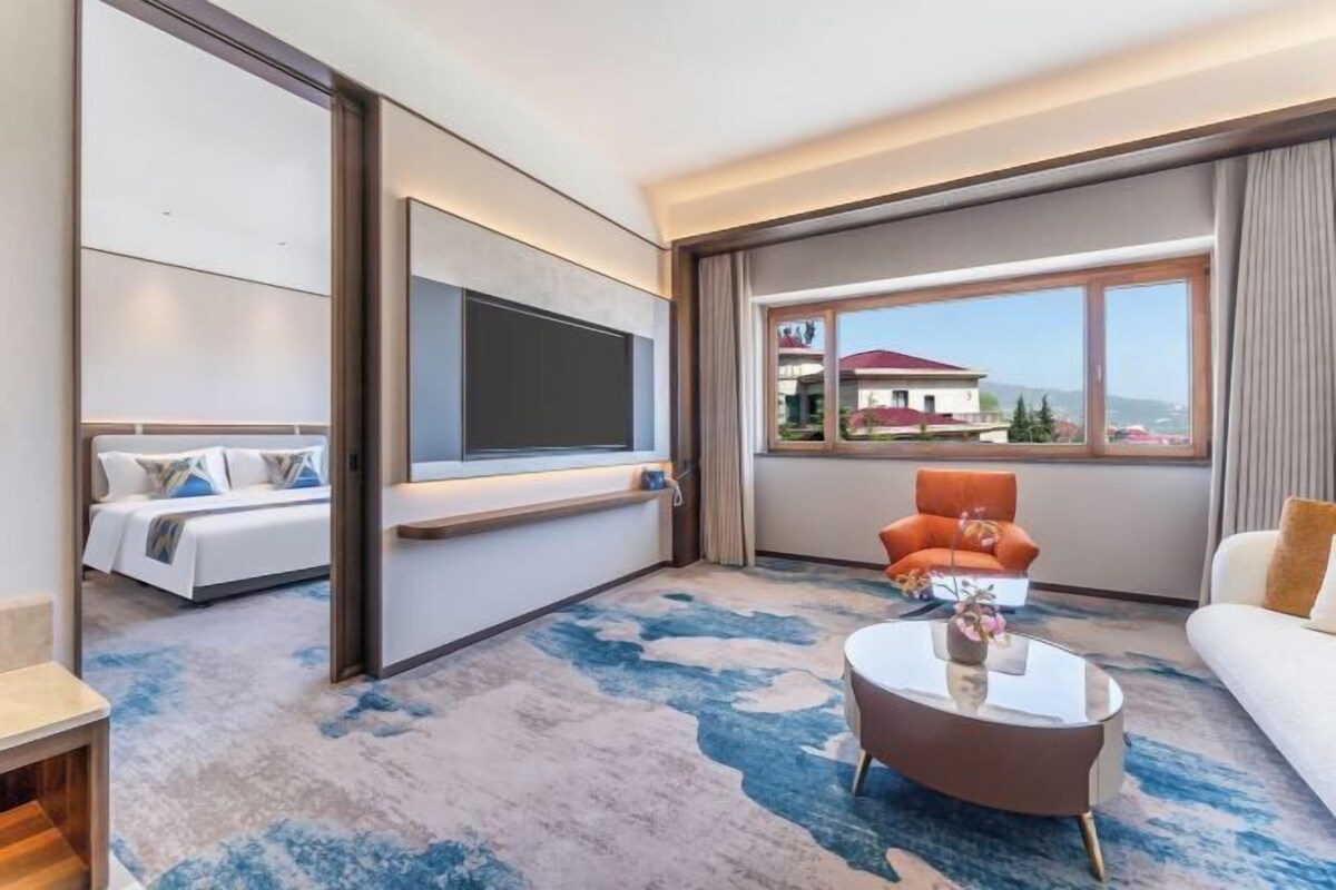 Een moderne hotelkamer met een bed, een televisie, een bank en een groot raam met uitzicht.