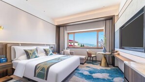 A hotel room with a large bed, a desk, a chair, a TV, and a window with a view. - Tarshan Hotel (WEIHAI)