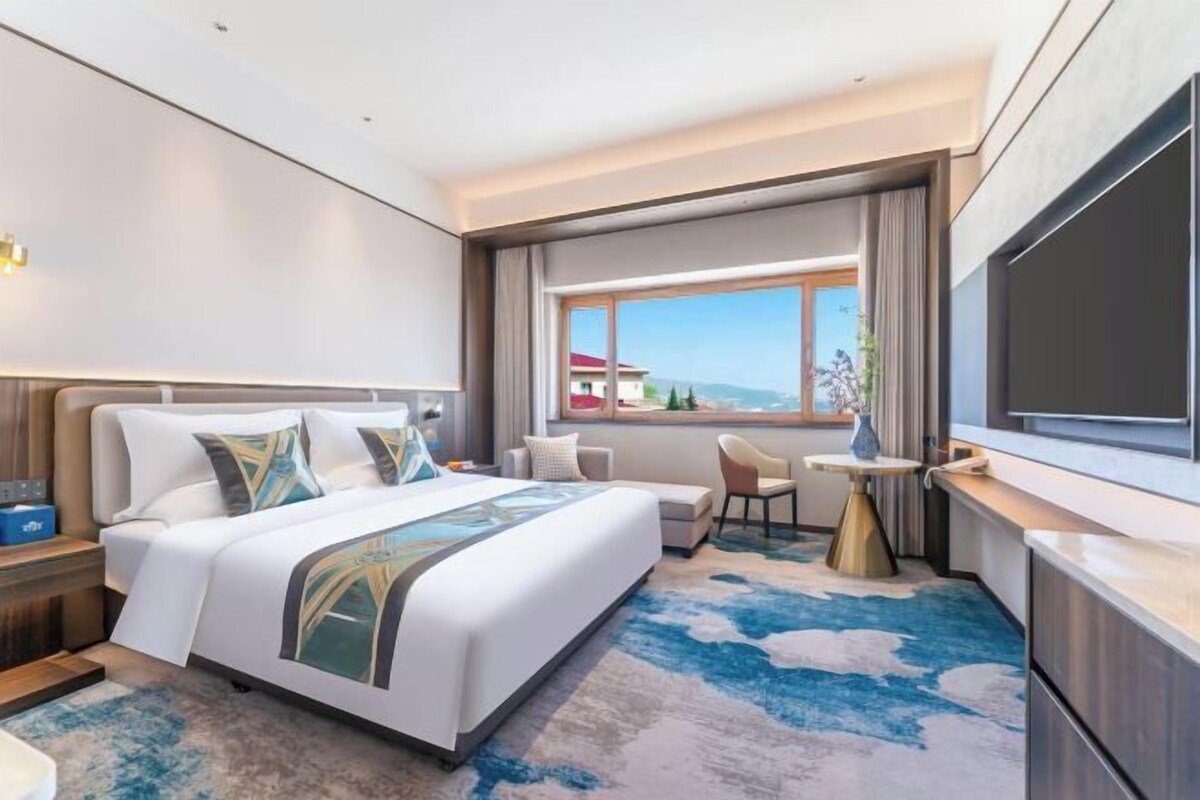 Een hotelkamer met een groot bed, een bureau, een stoel, een televisie en een raam met uitzicht.