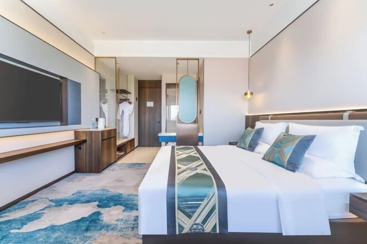 Een moderne hotelkamer met een groot bed, een flatscreen televisie, een inloopkast en een badkamer met een grote spiegel.