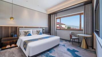 Habitación de hotel moderna con una cama grande, una mesita pequeña, una silla y un ventanal con vistas a edificios.