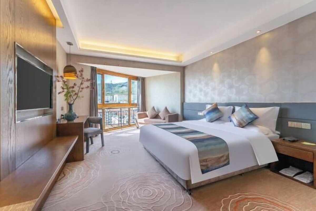 Een moderne hotelkamer met een groot bed, een televisie, een bureau en een balkon met uitzicht.