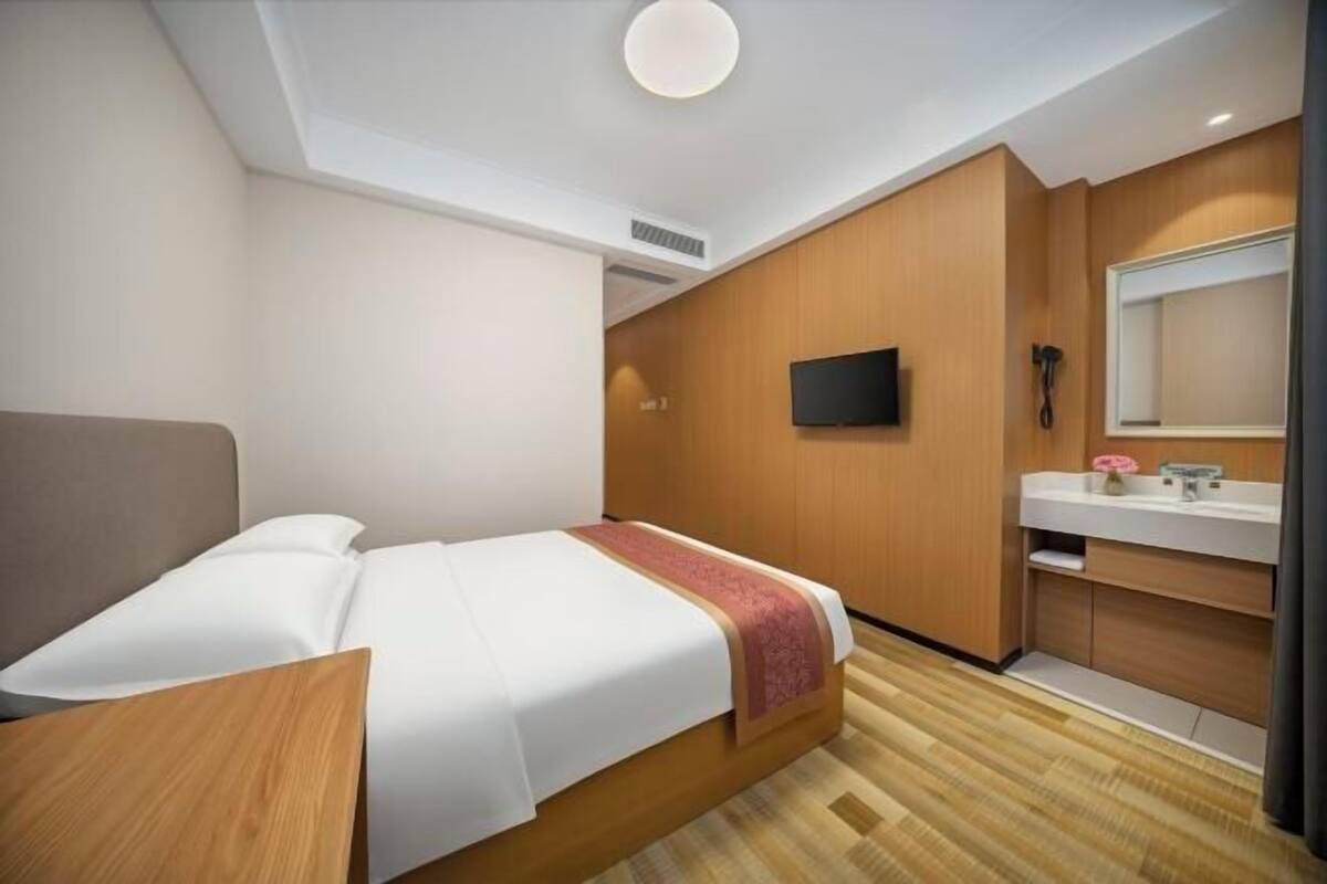 Een hotelkamer met een bed, nachtkastje, televisie, spiegel en een badkamer met een wastafel en spiegel.