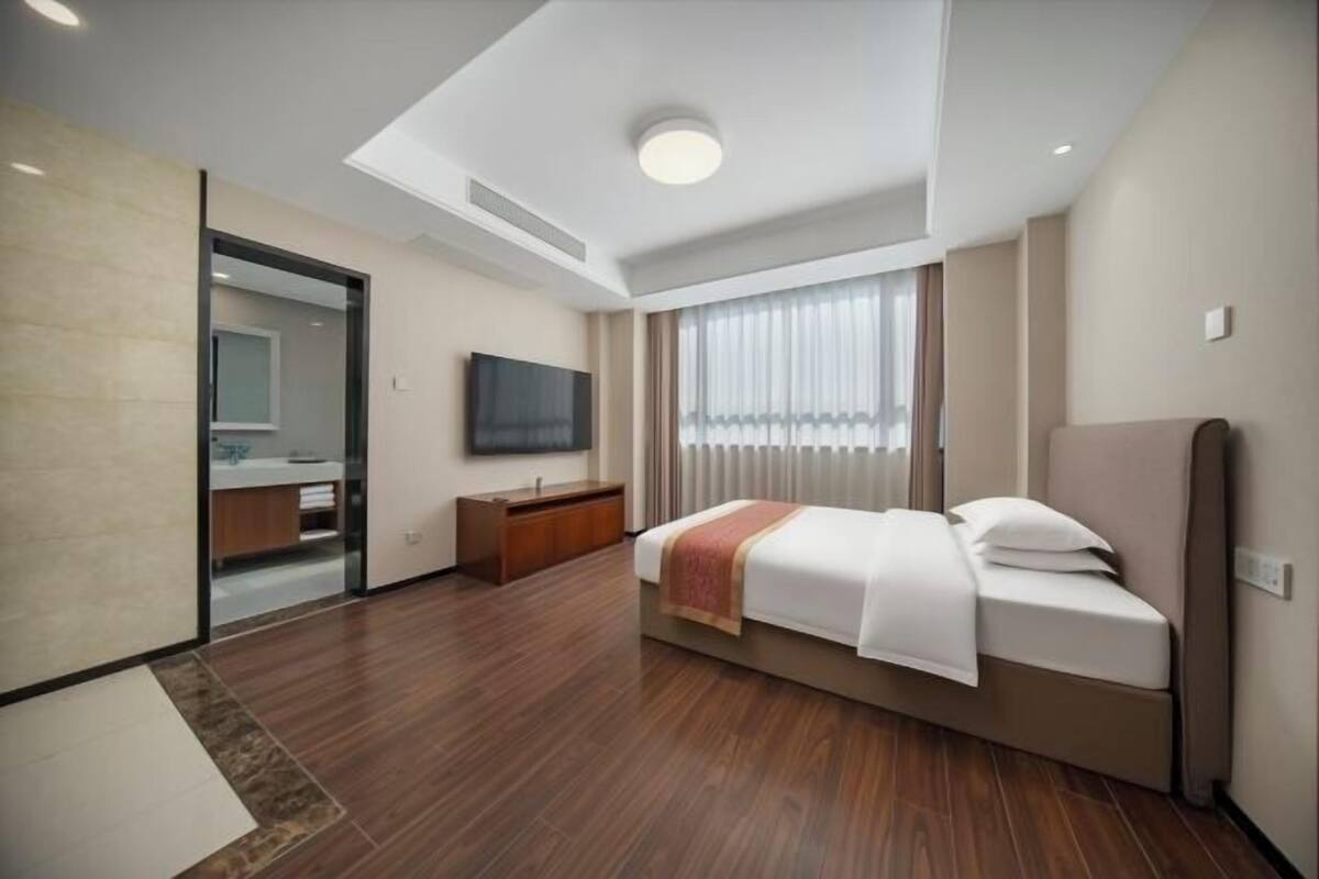 Een moderne hotelkamer met een bed, een televisie, een badkamer met een spiegel en een groot raam.