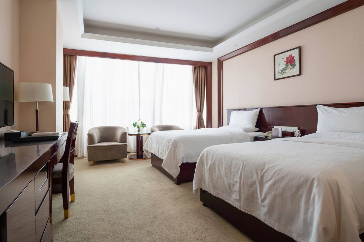 Een hotelkamer met twee bedden, een bureau, een stoel, een televisie en een raam met gordijnen.