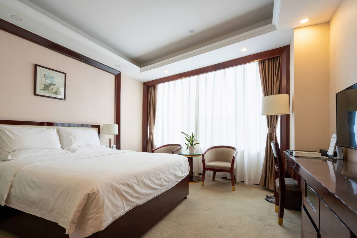 Een hotelkamer met een groot bed, een bureau met stoel, een televisie en een raam met gordijnen.