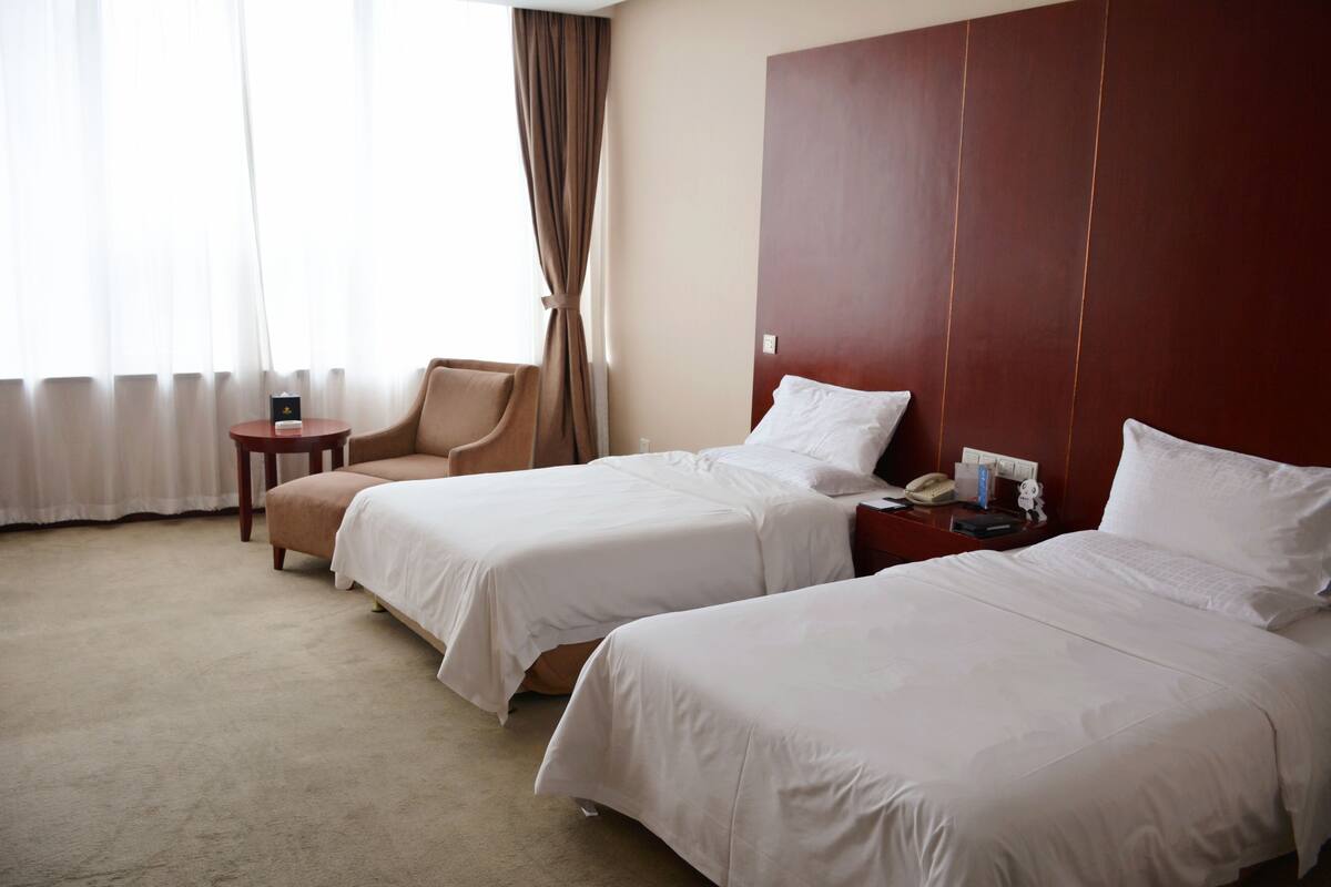 Een hotelkamer met twee enkele bedden, een stoel, een tafeltje en een nachtkastje met telefoon en lamp.