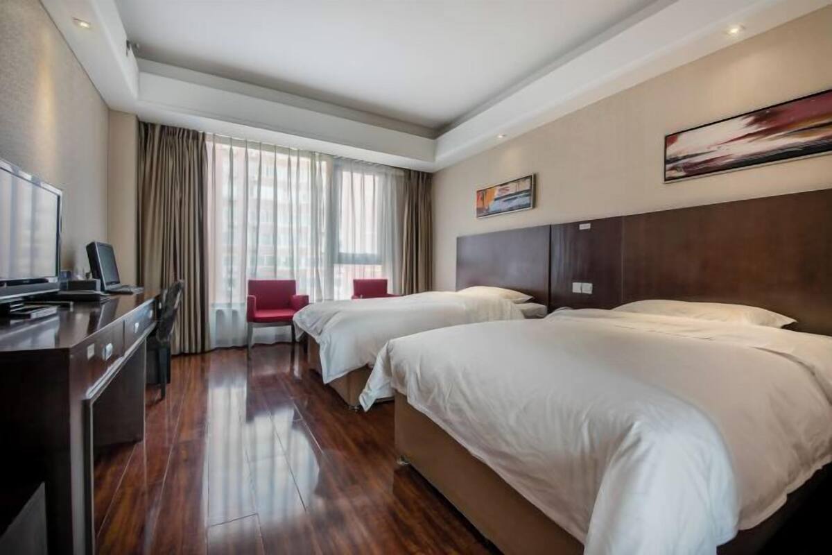 A hotel room with two beds, a desk, a chair, and a large window with curtains.