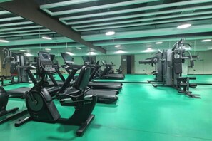 A gym with various exercise machines, a green floor, and a mirrored wall. - Beijing Henan Business Hotel (Beijing)
