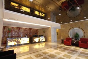A hotel lobby with a reception desk, two red chairs, a large mirror, and a patterned wall. - Beijing Henan Business Hotel (Beijing)