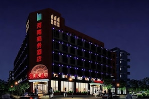 A multi-story hotel with a prominent entrance, illuminated signage, and a series of windows.