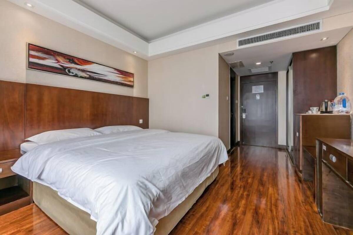 A hotel room with a large bed, wooden flooring, a painting on the wall, and a door leading to another room.