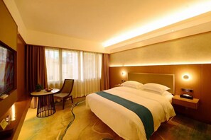 A hotel room with a bed, bedside table, lamp, chair, and a small table with a bowl of fruit. - Shenzhen Lotus Hotel (SHENZHEN)