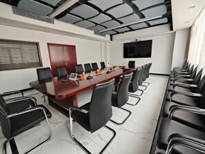 A conference room with a long table, multiple chairs, a flat-screen TV, and a large window with blinds. - Shenzhen Lotus Hotel (SHENZHEN)