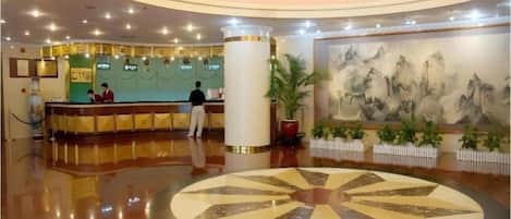 A hotel lobby with a reception desk, a large circular floor design, and a painting on the wall.