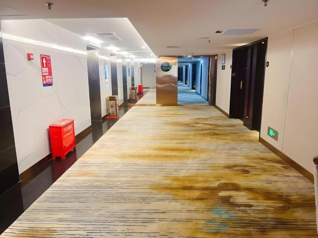 Un couloir d’hôtel avec un tapis à motifs, des portes des deux côtés et un panneau d’indication de sécurité incendie sur le côté gauche.