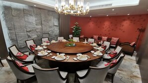Une table de salle à manger ronde, entourée de chaises, un lustre au plafond et, au fond, un canapé rouge recouvert de tissu.