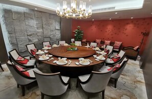 A round dining table with chairs, a chandelier, and a red upholstered sofa in the background.