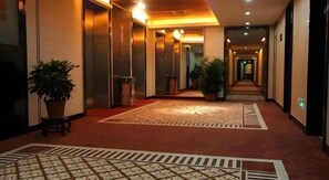 A hotel corridor with carpeted flooring, potted plants, and elevators. - Shenzhen Lotus Hotel (SHENZHEN)