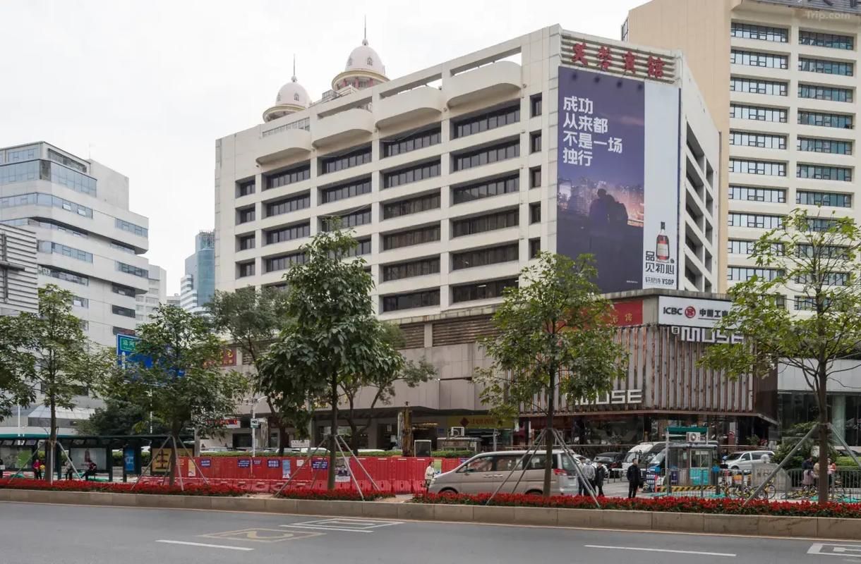 A multi-story building with a large billboard, surrounded by trees and a street with parked cars.