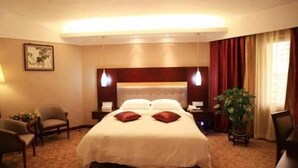 Une chambre d’hôtel avec un grand lit, des tables de chevet, une chaise, un bureau et une plante en pot.