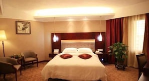 A hotel room with a large bed, bedside tables, a chair, a desk, and a potted plant.