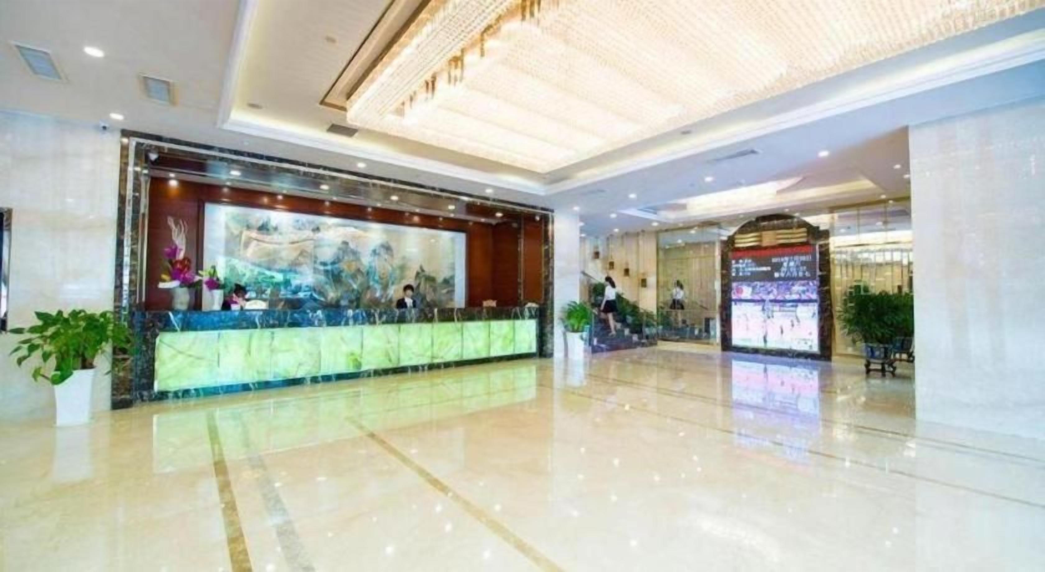A hotel lobby with a reception desk, a large digital screen, and a polished floor.