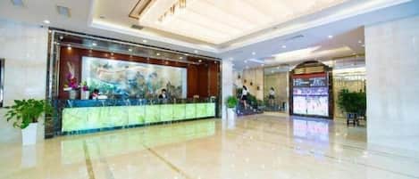 A hotel lobby with a reception desk, a large digital screen, and a polished floor.