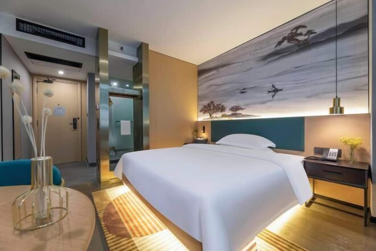 A modern hotel room with a large bed, a desk, a chair, and a painting on the wall.