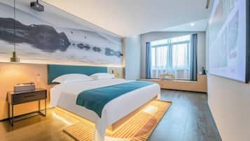 A modern hotel room with a large bed, a nightstand, a desk, a large window, and a wall-mounted projector.