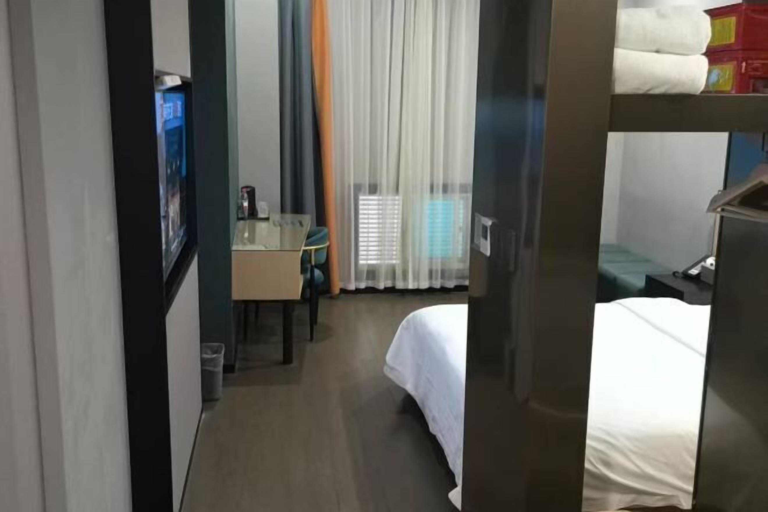A hotel room with a bed, a desk, a chair, and a window with curtains.