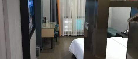 A hotel room with a bed, a desk, a chair, and a window with curtains.