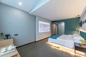 A modern hotel room with a bed, a massage table, a projector screen, and a small desk with a plant. - Nanyuan Ejiaplus Hotel (Ninghai Xizi International) (NINGHAI)