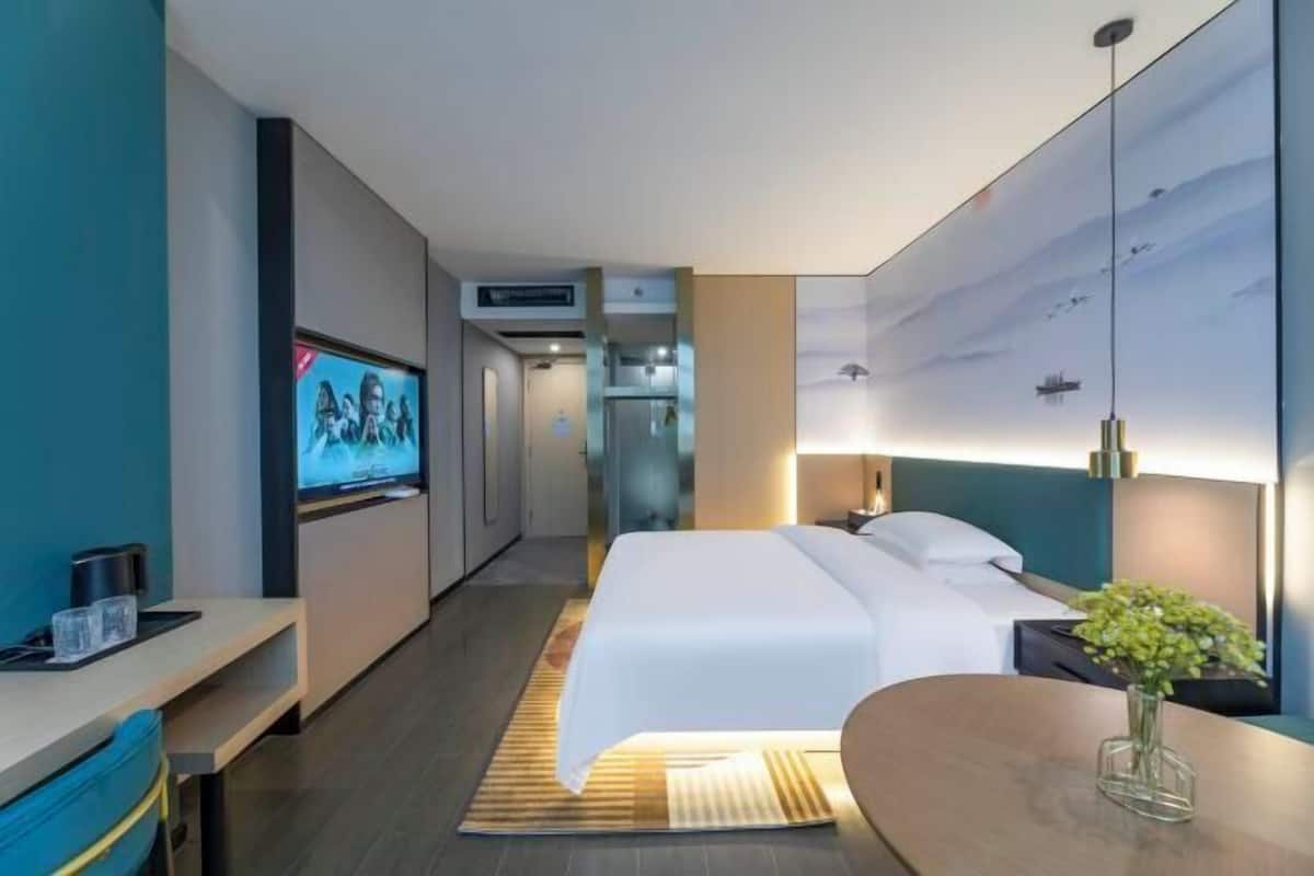 A hotel room with a bed, bedside table, TV, and a view of the hallway.