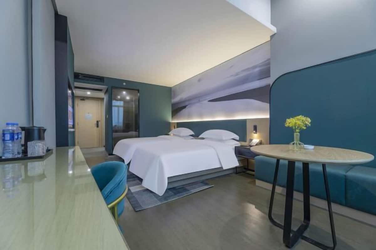 A modern hotel room with a bed, a round table, a sofa, and a wall-mounted TV.