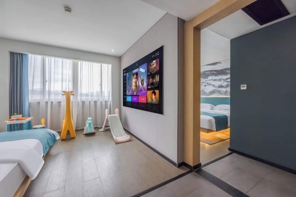 A modern hotel room with a large TV, a bed, a desk, and a view of a snowy landscape.
