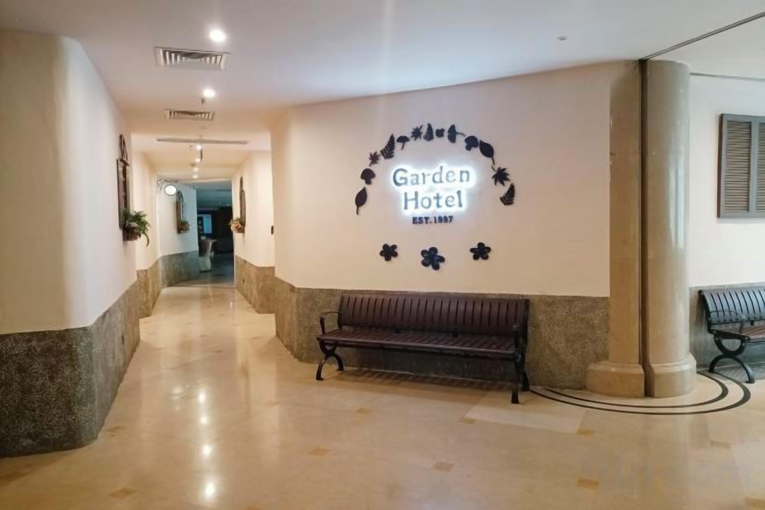 En hotellobby med en receptionsdisk, en bänk och en väggskylt med texten ”Garden Hotel”.