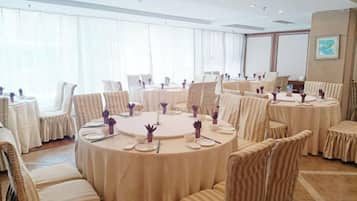 A conference room with round tables and chairs, large windows with sheer curtains, and a framed picture on the wall.