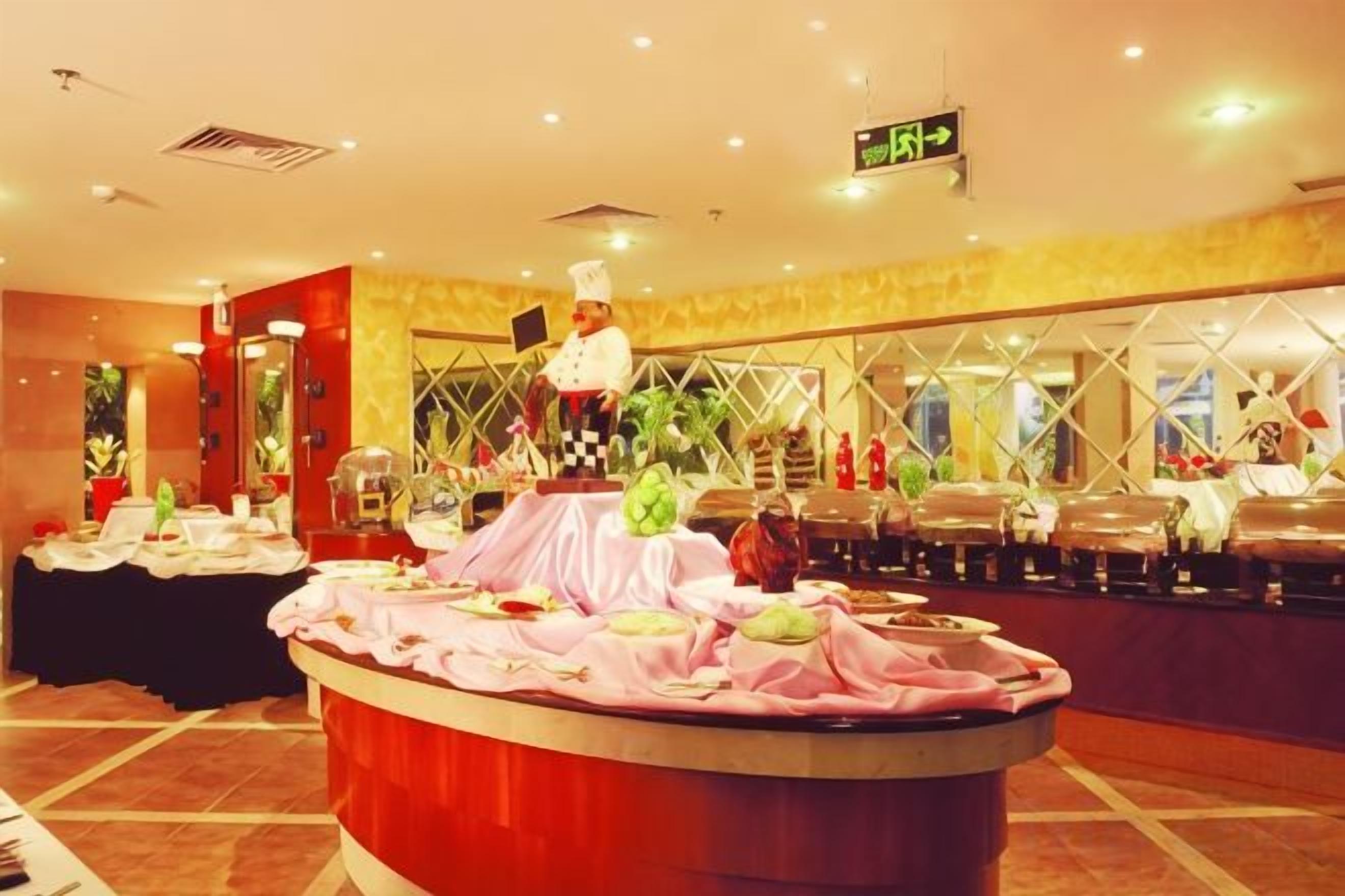 A buffet setup with a chef, a round table with food, and a buffet counter in a well-lit room with a patterned wall and a ceiling sign.