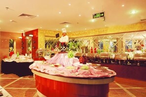 A buffet setup with a chef, a round table with food, and a buffet counter in a well-lit room with a patterned wall and a ceiling sign. - South Garden Hotel (Chongqing)