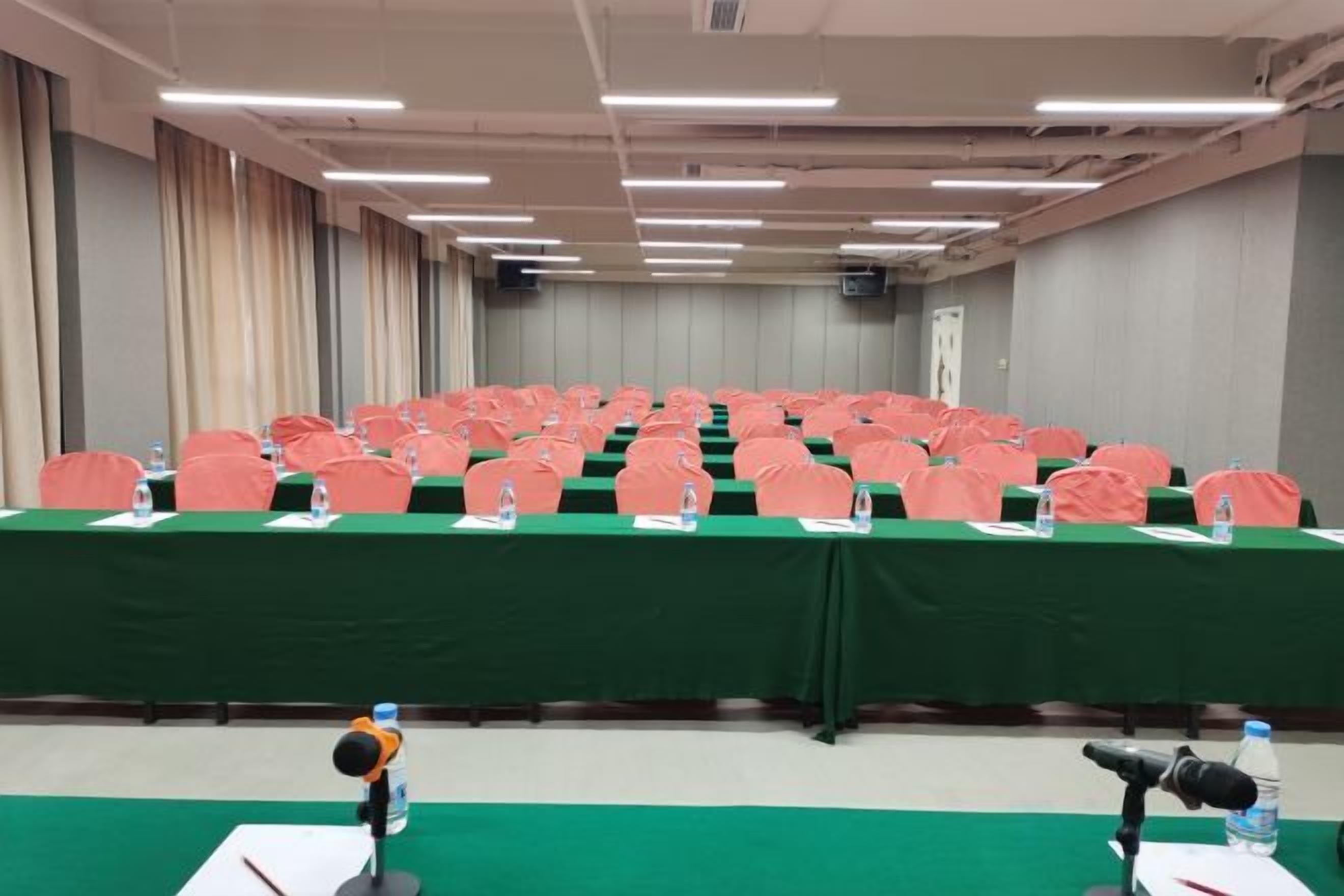 Een vergaderzaal met rijen tafels, stoelen en microfoons.
