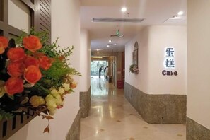 A hallway with a reception area, a sign indicating a cake shop, and a potted plant with flowers. - South Garden Hotel (Chongqing)