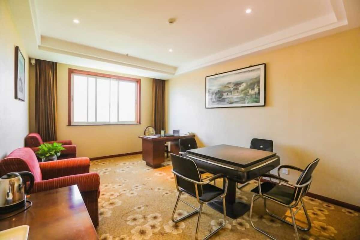 A hotel room with a large window, a dining table with chairs, a sofa, and a desk with a computer.