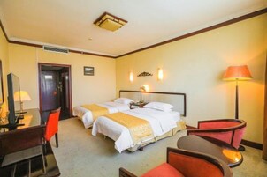 Quarto de hotel com duas camas, uma escrivaninha, uma cadeira e um abajur.